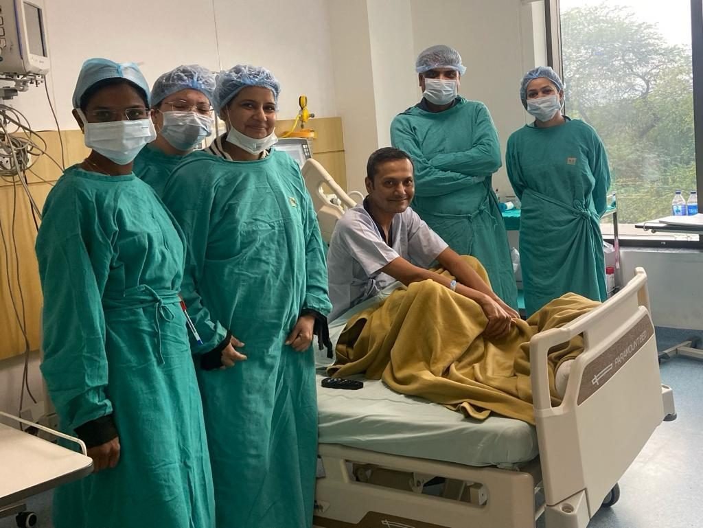 Patient sitting up in the liver transplant ICU surrounded by the transplant team in gowns and caps